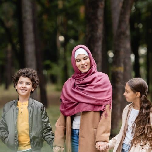 Muslim woman in hijab holding hands of children in park